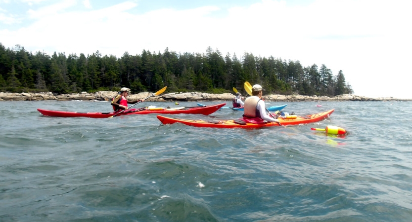 Two people wearing life jackets paddle red kayaks